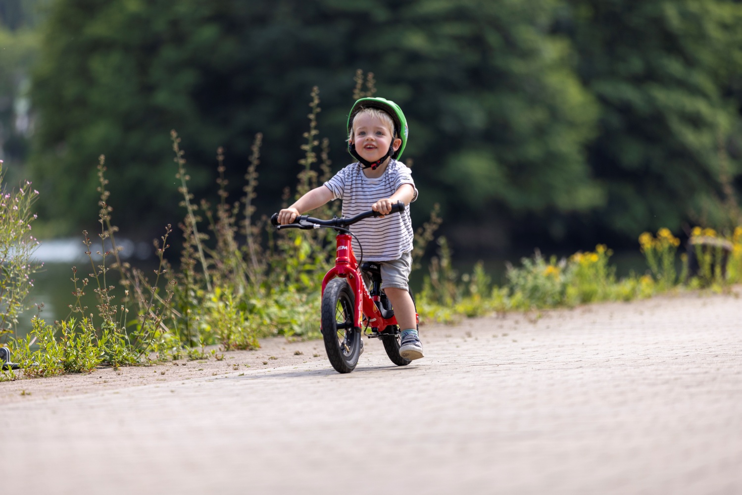 Berniukas važiuojantis raudonu balansiniu dviraiču